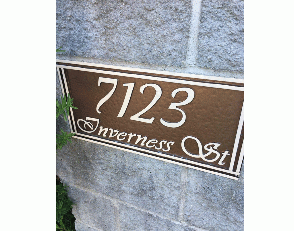 Brown rectangular 7123 Inverness St address sign with light lettering mounted on a grey masonry wall