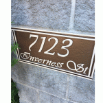 Brown rectangular 7123 Inverness St address sign with light lettering mounted on a grey masonry wall