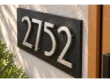 Angled close-up of stainless steel 2752 numbers showing mounting spacers above a textured black slate address plaque.