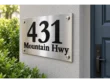 Right angled view of a brushed stainless steel 431 Mountain Hwy address plaque on a stucco wall beside a blue door.
