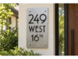 Vertical brushed stainless steel address plaque reading 249 WEST 16TH in black lettering on a cream stucco wall.