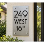 Vertical brushed stainless steel address plaque reading 249 WEST 16TH in black lettering on a cream stucco wall.