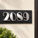 Black slate address plaque with raised silver stainless steel 2089 numbers beside a wooden entrance door.