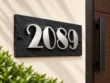 Left-angle view of a black slate 2089 address sign showing raised stainless steel numbers and textured stone.