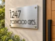 Right angled view of a brushed metal cut-out address plaque reading 1247 FOXWOOD CRES. beside a wooden front door.