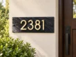 Left-angle view of a dark stone 2381 address plaque showing its textured surface and raised gold-coloured numbers.