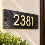 Dark Stone Address Sign with Gold-Coloured Numbers - Dark textured stone address sign with raised gold-coloured 2381 numbers beside a wooden entrance door.