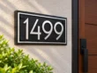 Left angled view of a matte black 1499 address plaque with raised silver numbers, silver border and black corner fixings.