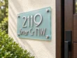 Left-angle view of a frosted glass address plaque reading 2119 Briar Cr NW in raised silver lettering.