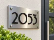 Left angled view of a brushed stainless steel address plaque showing the depth of raised black 2053 numbers.