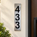 Slim stainless steel house number sign displaying 433 vertically on a cream wall beside a wooden entrance door.