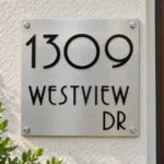 Square Stainless Steel Address Sign with Raised Black Lettering - Square brushed stainless steel address sign with raised black 1309 WESTVIEW DR lettering beside a wooden entrance door.