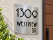 Left angled view of a stainless steel 1309 WESTVIEW DR address plaque showing raised black lettering and silver corner fixings.