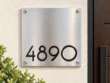 Square Stainless Steel Address Sign with Low-Set Numbers - Square brushed stainless steel address sign with black 4890 numbers positioned near the bottom, beside a wooden door.