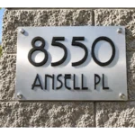 Brushed stainless steel address plaque with raised black 8550 and ANSELL PL lettering mounted on a stone pillar.