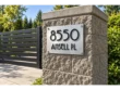 Angled view of a brushed stainless steel 8550 ANSELL PL address sign on a stone pillar beside a dark driveway gate.