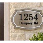 Shaped metallic-coloured address plaque with dark 1254 Dempsey Rd lettering and a light decorative inner border
