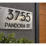 Brushed silver address plaque with floating black 3755 numbers and PANDORA ST lettering beside a wooden entrance door.