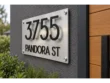 Close-up of floating black house numbers casting shadows on a brushed silver address plaque.
