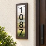 Vertical Stainless Steel Address Sign on Wood Backing - Vertical stainless steel address sign with black 1087 numbers on dark wood backing beside a wooden entrance door.
