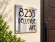 Right-angle view of a brushed stainless steel address plaque reading 8253 Bellevue Ave on a cream exterior wall.