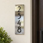 Vertical Brushed Stainless Steel Number Plaque - Vertical brushed stainless steel plaque displaying black 2548 numbers beside a wooden entrance door.