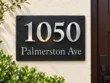 Right-angle view of a black slate plaque with silver 1050 numbers and Palmerston Ave lettering on a cream wall.