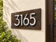 Left-angle view of a brown slate 3165 address plaque showing floating aluminium numbers and textured stone.