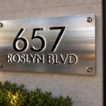 Close-up of a brushed silver address plaque with black “657 Roslyn Blvd” lettering and white halo lighting.
