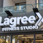 Lagree X Fitness Studio custom channel letter sign with white dimensional letters mounted on dark brick beneath a glass canopy.