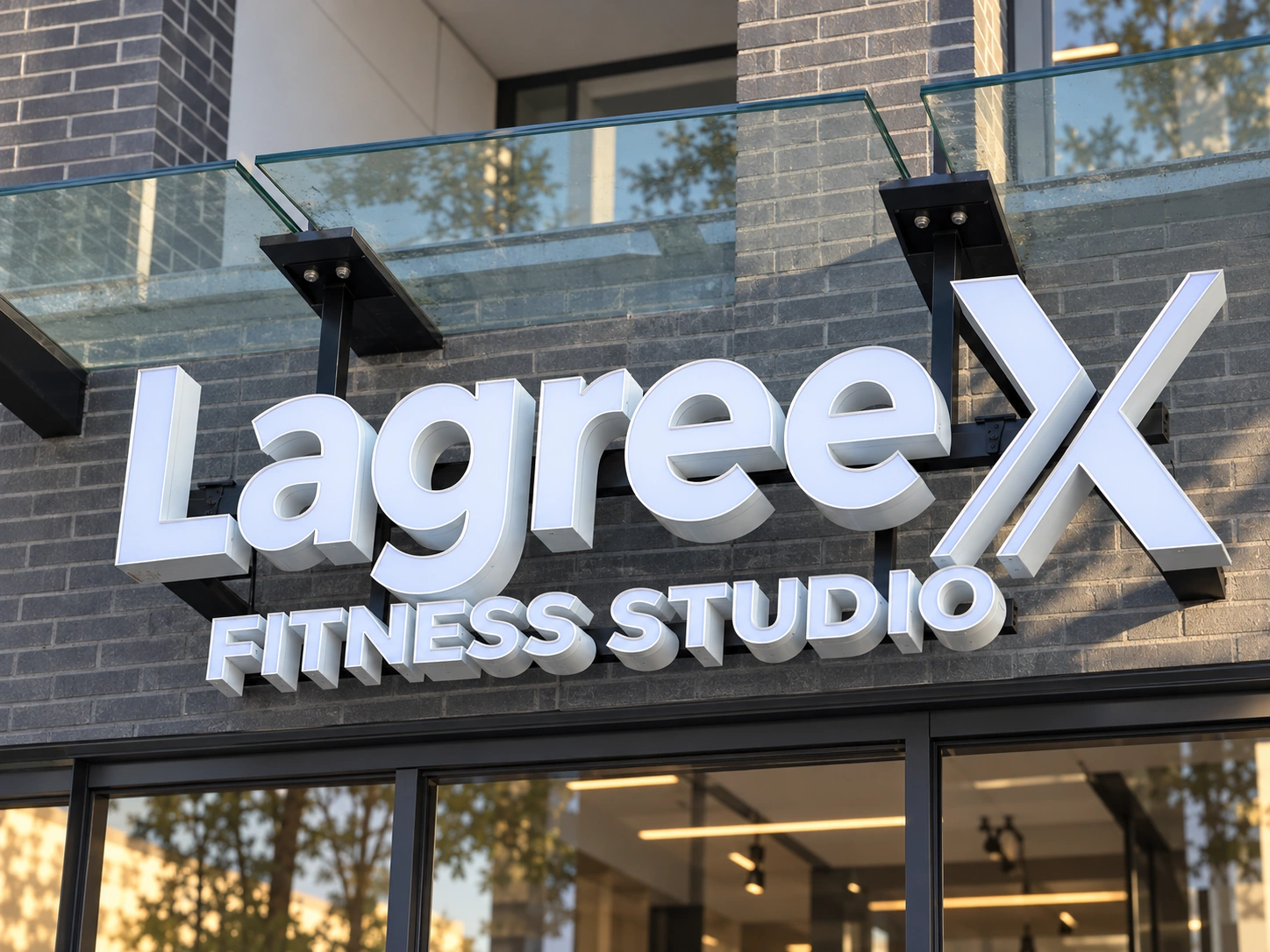 Custom Channel Letter Sign – Lagree X Fitness Studio Lagree X Fitness Studio custom channel letter sign with white dimensional letters mounted on dark brick beneath a glass canopy.