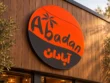 Abadan custom round lightbox sign with orange and charcoal graphics and English and Persian lettering mounted on wood storefront cladding.