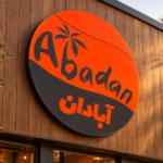 Abadan custom round lightbox sign with orange and charcoal graphics and English and Persian lettering mounted on wood storefront cladding.