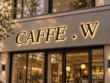 Caffe W backlit channel letter sign with black serif letters and warm halo illumination on a light-coloured storefront façade.
