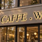 Caffe W backlit channel letter sign with black serif letters and warm halo illumination on a light-coloured storefront façade.