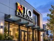 Wider view of the NIO Exchange sign above a glass-canopy entrance on a modern commercial facade at dusk.