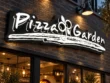 Angled close-up of Pizza Garden’s illuminated white script, decorative motif, and textured underline on black backing.
