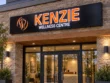 Angled close-up of Kenzie’s orange lettering with white illuminated outlines and an orange logo against a black light box face.