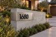 Bent brushed stainless steel corner address sign 1680 with raised black numbers on a low concrete entrance wall