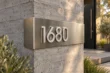 Bent stainless steel address sign 1680 with raised brushed silver numbers wrapping a concrete wall edge
