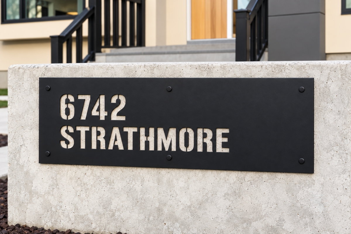 Close-up of black aluminium sign with 6742 Strathmore cut through the panel, revealing concrete behind