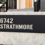 Close-up of black aluminium sign with 6742 Strathmore cut through the panel, revealing concrete behind