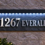 Front view of a natural slate address sign with raised 1267 EVERALL lettering, black corner fixings and LED lights beneath a black hood.