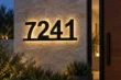 Black 7241 house numbers connected along a bottom bar with warm halo lighting on a stone entrance wall.