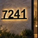 Black 7241 house numbers connected along a bottom bar with warm halo lighting on a stone entrance wall.