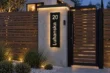 Black vertical aluminium address sign with illuminated 20 Luhanska lettering and warm edge lighting on a gate pillar.