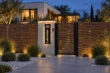 Illuminated vertical 20 Luhanska address sign on a pillar beside a wood slat gate at a landscaped modern home.