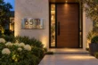 Backlit stainless steel 6571 WHITE OAK DR address plaque beside a wood front door at a landscaped home entrance.