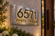Angled close-up of raised black 6571 WHITE OAK DR lettering with warm backlighting on a brushed stainless steel panel.