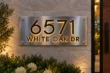 Front view of a brushed stainless steel plaque with raised black 6571 WHITE OAK DR lettering and warm halo backlighting.